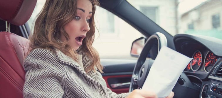Young girl sitting inside of a car and reading fine papers, looking frustrated.