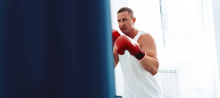 middle-aged boxer training in a gym, fighting with punching bag close up