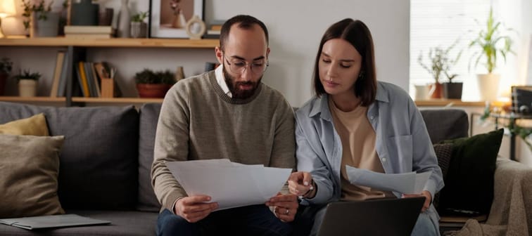 Busy middle-aged couple reviews and discusses their finances on a couch in a home setting.