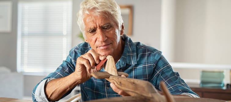 Retired man using sandpaper to polish wooden airplane sculpture.