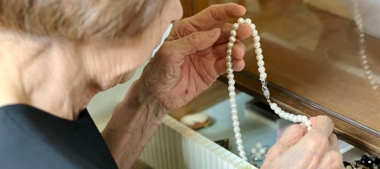 Elderly woman in mourning dress taking out pearl necklace from drawer