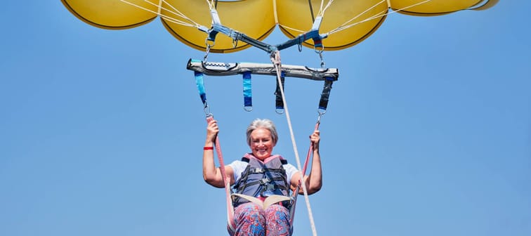 Woman with gray hair with a big smile and a fearless expression parasailing.