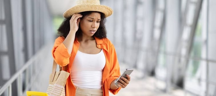 A young Black woman in an airport, looking at her phone with concern