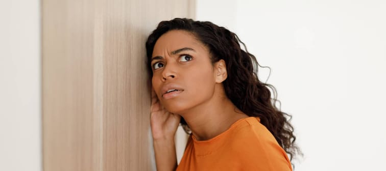 Young black woman listening at the neighbour's wall