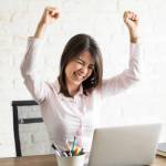 Excited woman using the computer and celebrating some good news with her arms up